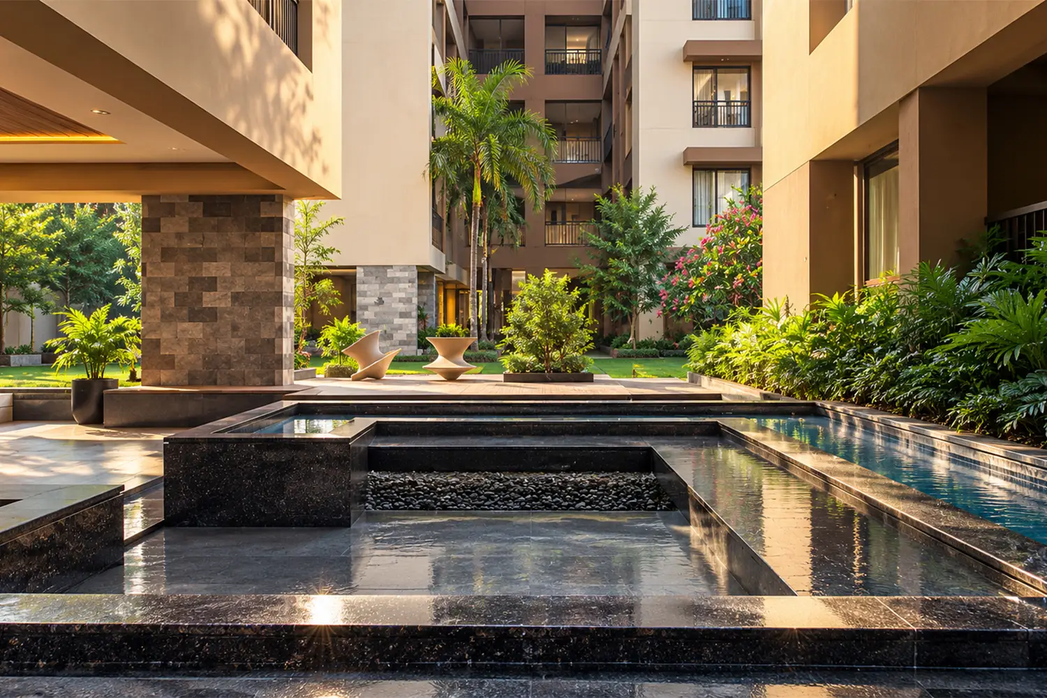 The Pravya’s landscaped courtyard featuring a serene water feature, lush tropical greenery, elegant seating areas, and contemporary residential architecture in warm natural light.